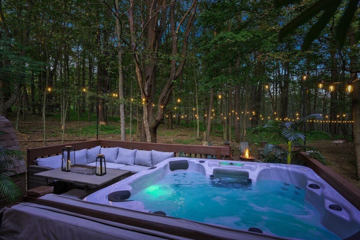 A hot tub surrounded by a wooden deck, with string lights and a fire pit.