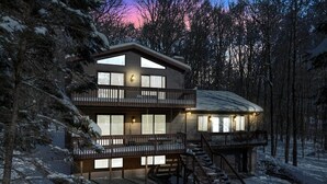 A two-story cabin with a balcony, surrounded by snow-covered trees.