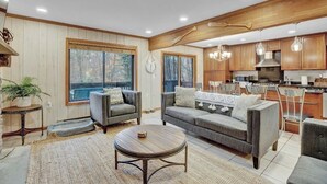 A spacious living room with a grey sofa, a round coffee table, and a view of the outdoors through large windows.