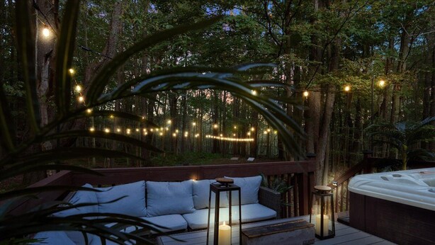 A deck with a sofa and two lanterns, surrounded by trees and string lights.
