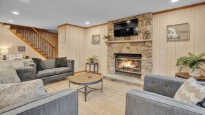 A living room with a stone fireplace, grey sofas, a coffee table, and a staircase.