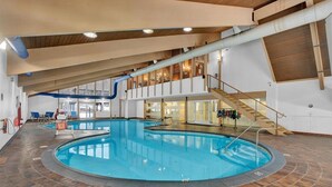 An indoor swimming pool with a tiled floor, a wooden ceiling, and a staircase leading to an upper level.