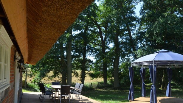 Una terraza de madera con mobiliario exterior, un espacio cubierto con una mesa y sillas, y un pabellón.