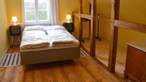 Un dormitorio con cama, dos lámparas de noche, una ventana con cortinas, un armario de madera y un radiador.