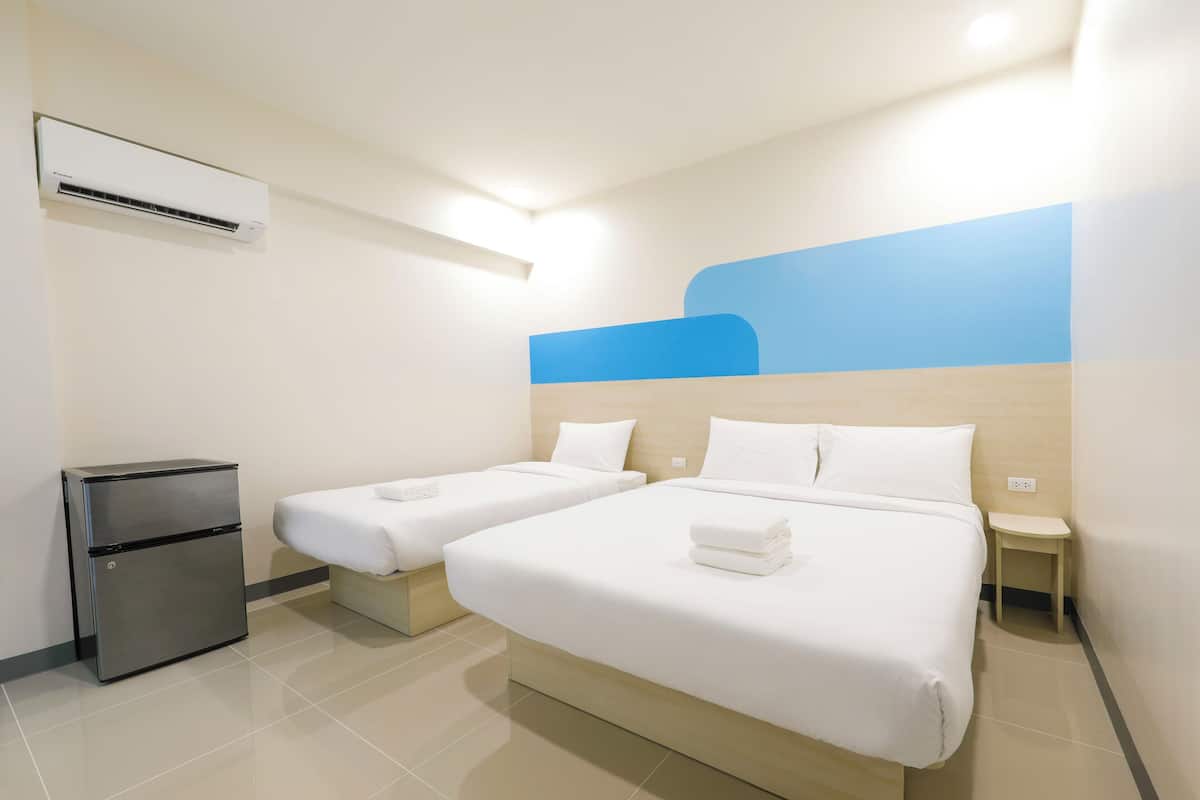 Ein Hotelzimmer mit zwei Einzelbetten, einem kleinen Kühlschrank, einem Nachttisch und einer Klimaanlage.