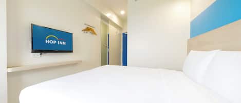 Una habitación de hotel moderna con una cama grande, un televisor montado que muestra el logotipo de 'Hop Inn' y una pared azul decorativa.