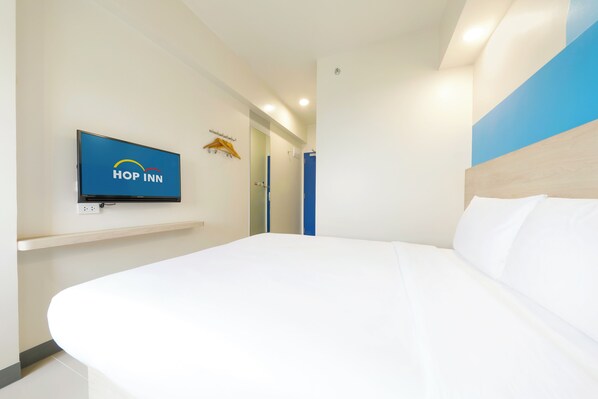 Una habitación de hotel moderna con una cama grande, un televisor montado que muestra el logotipo de 'Hop Inn' y una pared azul decorativa.
