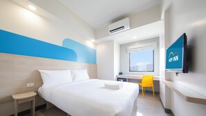 Une chambre d’hôtel moderne équipée d’un lit, d’un bureau, d’une chaise et d’un téléviseur fixé au mur.
