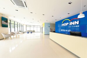 Un área de recepción moderna de hotel con una pared azul, un mostrador de recepción y una zona de estar.