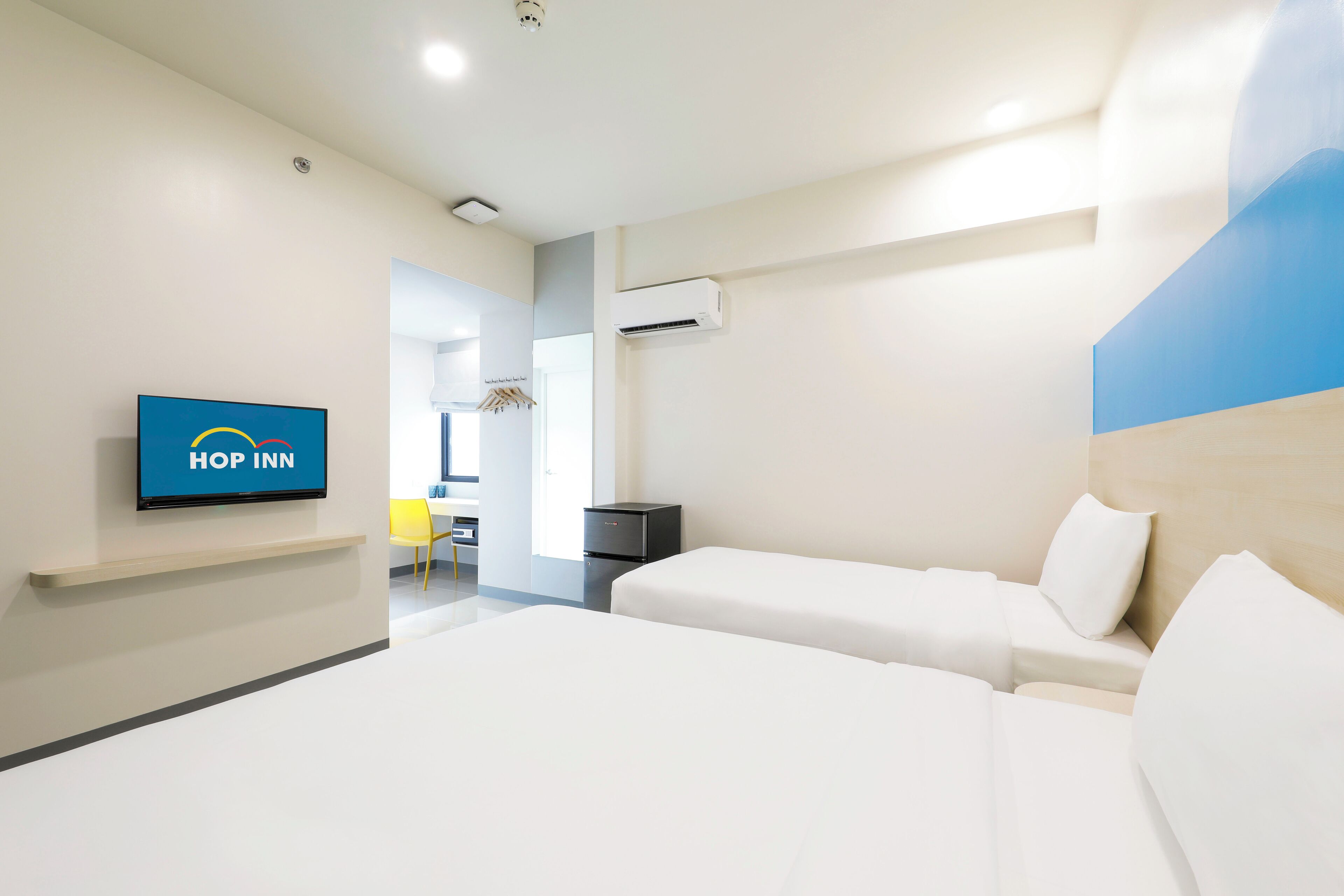 Moderni hotellihuone, jossa on kaksi sänkyä, televisio, jossa näkyy hotelliketjun logo, ja selkeästi erotettavissa oleva kylpyhuonealue.