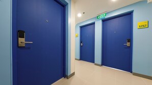 Un couloir avec des portes bleues, un panneau indiquant la sortie et le numéro de la pièce : 1212.