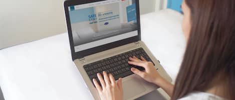 A person using a laptop on a bed with a white mattress and a blue wall in the background.