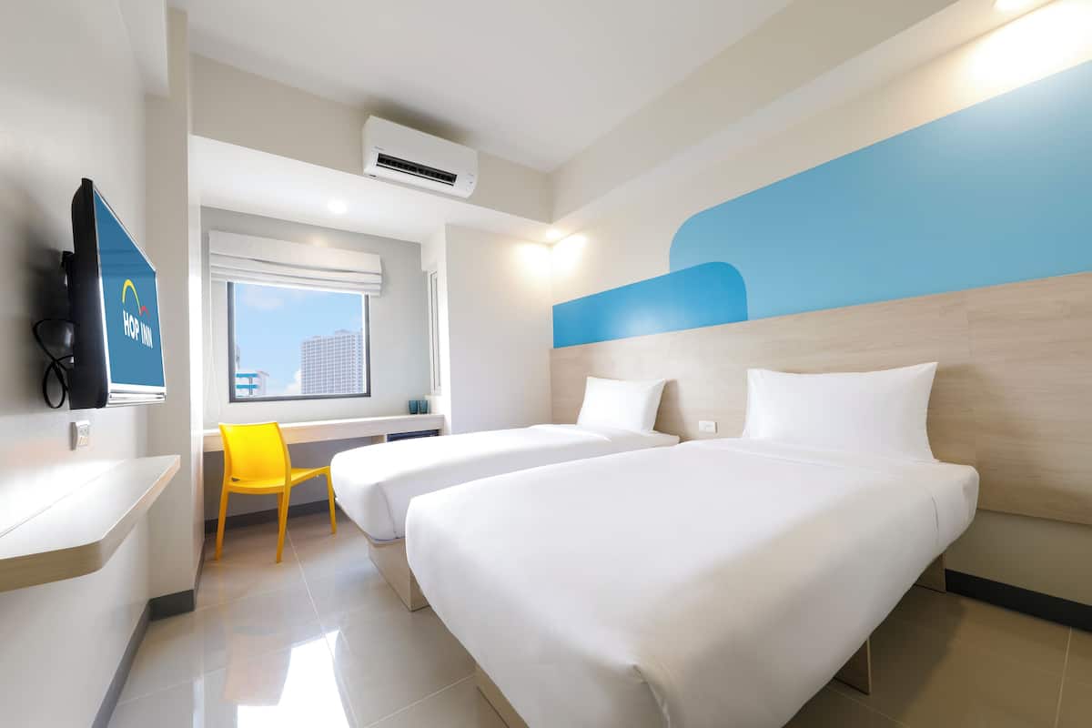 Ein Hotelzimmer mit zwei Betten, einem Schreibtisch, einem Stuhl und einem Fernseher.