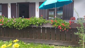A wooden fence with flower boxes, a blue umbrella, and yellow flowers in a garden area. - Reindler Modern Retreat (Fischen im Allgaeu)
