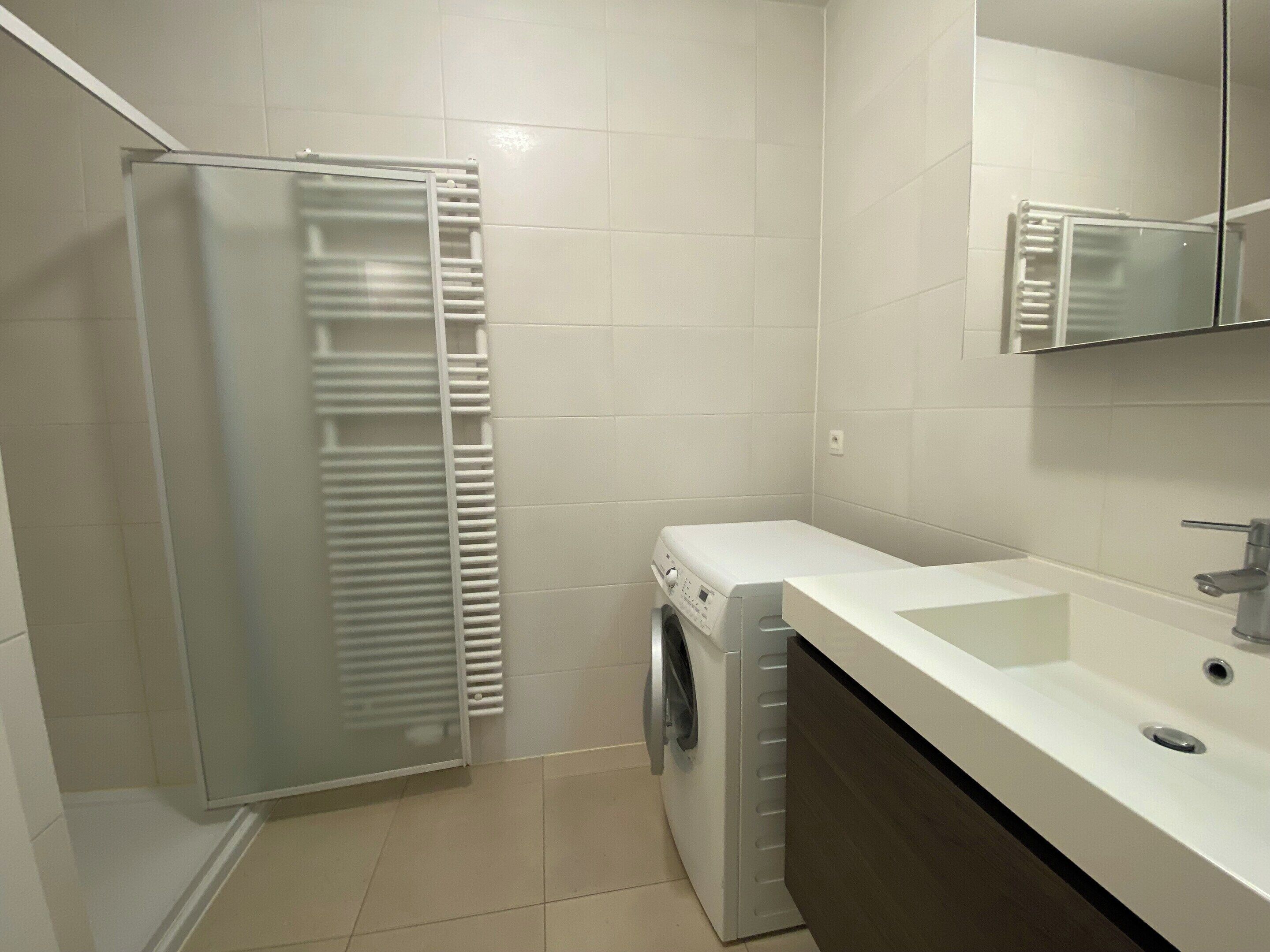 A compact bathroom with a washing machine, a sink, and a glass shower enclosure.