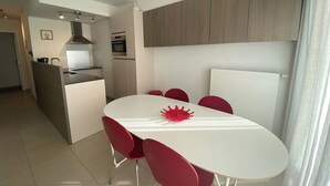 A modern kitchen with a central island, a dining area with a white table and red chairs, and a view of the living area. - Apartment in Nieuwpoort Near the Beach (Nieuwpoort)
