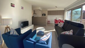 A modern living room with a TV, blue and black sofas, a dining area with red chairs, and a kitchen in the background. - Apartment in Nieuwpoort Near the Beach (Nieuwpoort)
