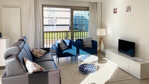 A modern living room with a sofa, chairs, a TV, and a balcony view. - Apartment in Nieuwpoort Near the Beach (Nieuwpoort)