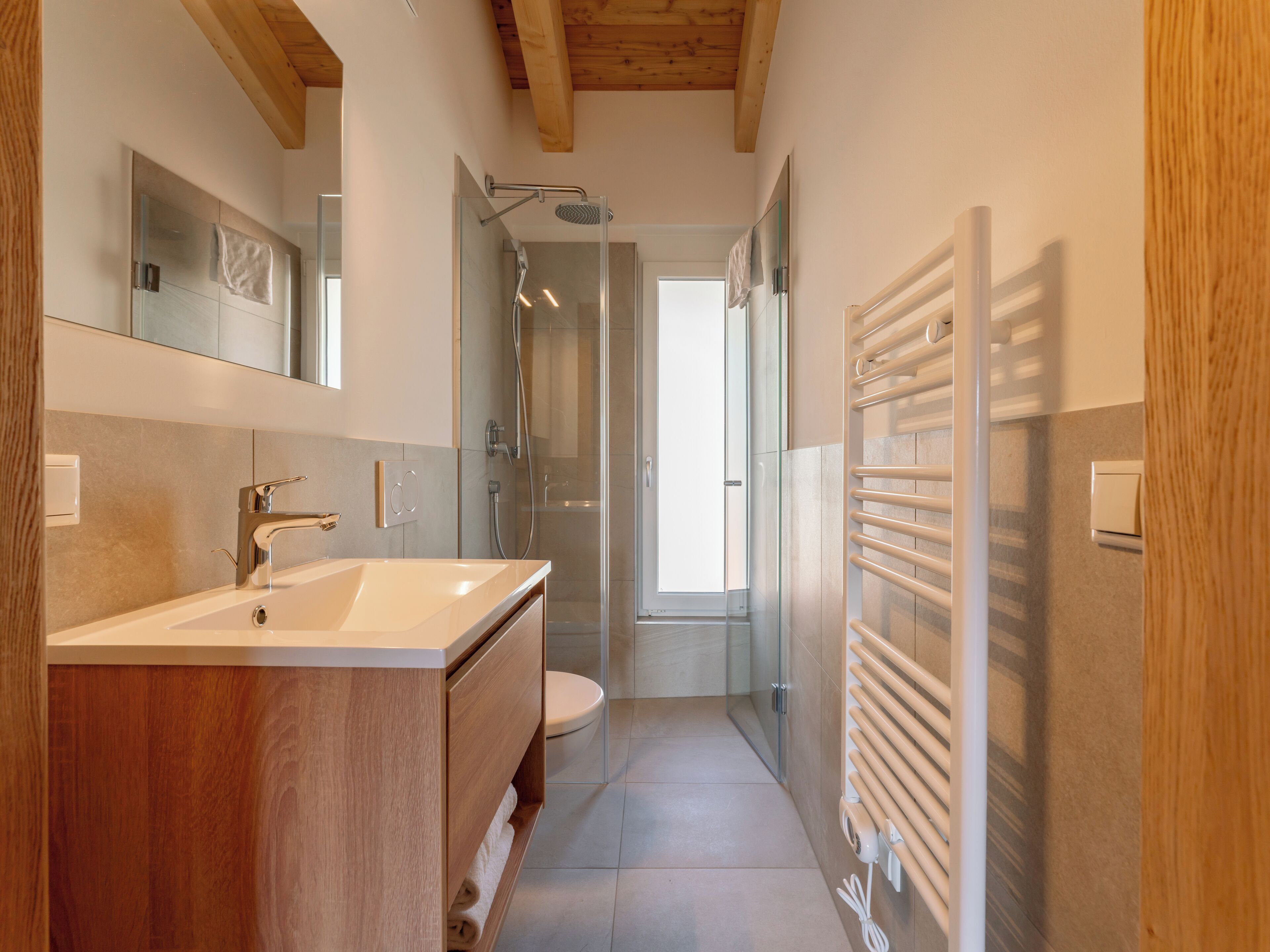 A modern bathroom with a wooden vanity, a glass shower enclosure, and a towel rack.