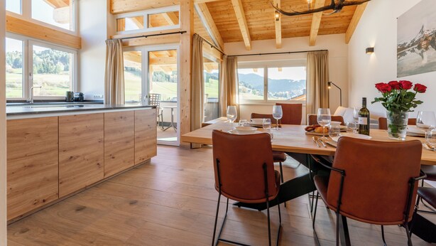 Un intérieur en bois comprenant une table à manger pour quatre personnes, un coin cuisine et de grandes fenêtres donnant sur l’extérieur.