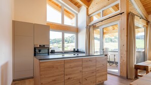 Une cuisine moderne avec des meubles en bois, un grand îlot central et une vue sur un paysage verdoyant grâce à de grandes fenêtres.