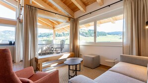 A cozy room with a wooden ceiling, a large window with a view of a green landscape, a red chair, a grey sofa, and a small round table. - Spacious home located directly at the slopes (Sankt Lambrecht)