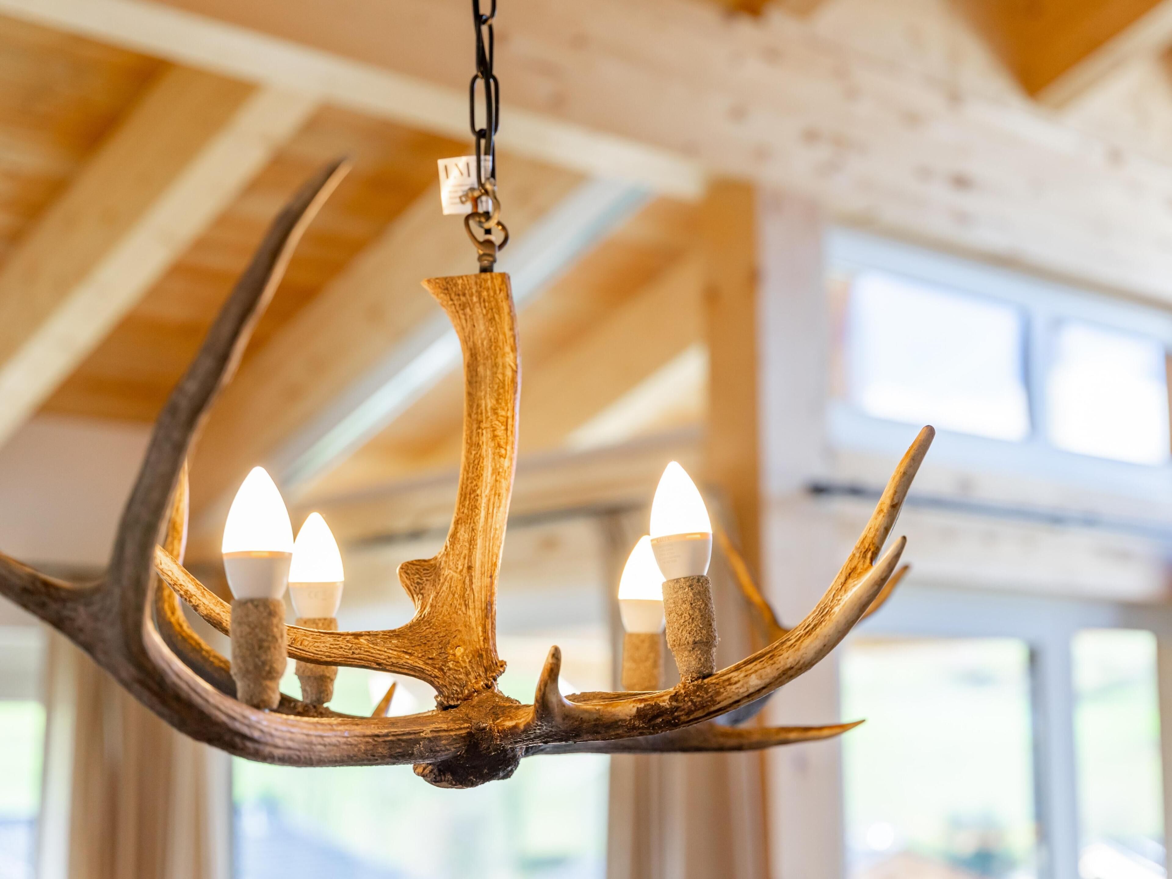 Un lustre à trois lampes, fabriqué à partir de bois de cerf, suspendu à un plafond avec des poutres en bois.