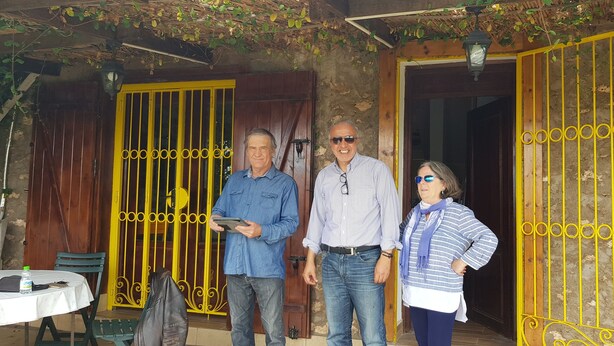 Three people standing outside a building with yellow gates and a table with a bottle and a bag. - Maison la branche d oiseaux (Douar Driss)
