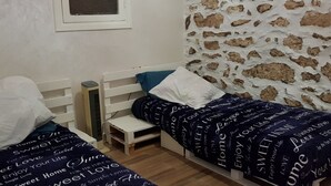 A bedroom with two single beds, a small bedside table, a heater, and a stone-patterned wall. - Maison la branche d oiseaux (Douar Driss)