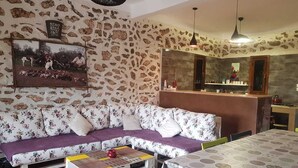 A living room with a stone wall, a sofa, a coffee table, and a dining table. - Maison la branche d oiseaux (Douar Driss)