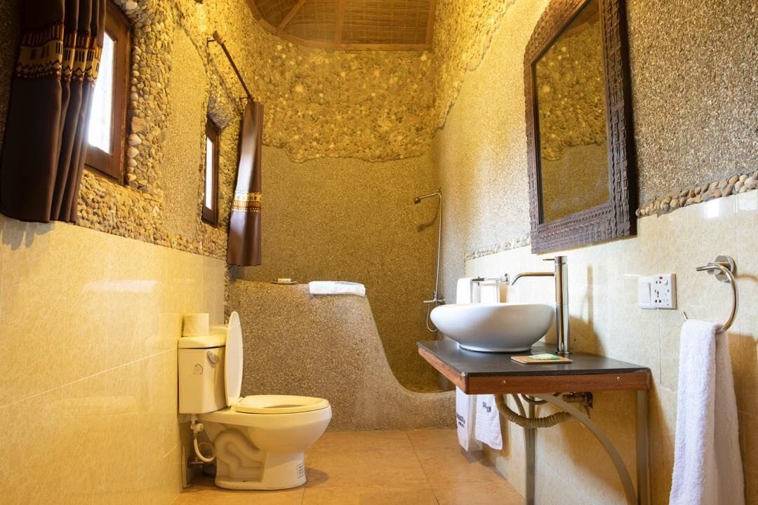 Une salle de bain avec un mur en pierre, des toilettes blanches, un lavabo avec un receveur et un miroir.