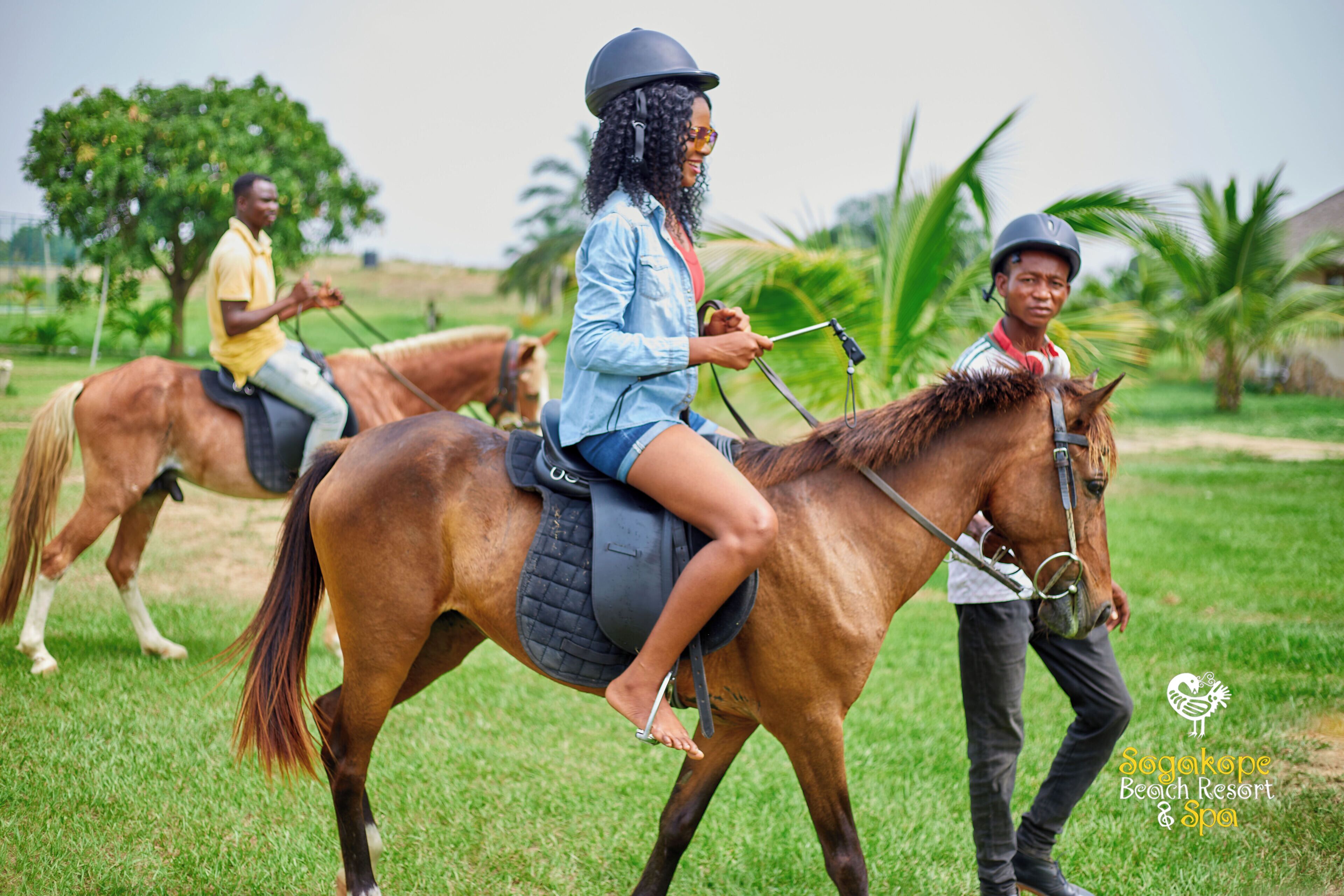 Trois personnes à cheval évoluent sur un champ herbeux, et on peut voir le logo de « Sogakoppe Beach Resort & Spa ».