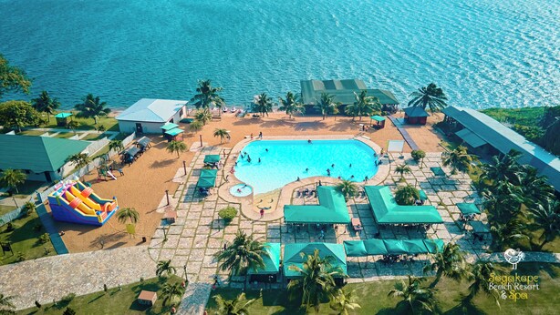 An aerial view of a beach resort with a large swimming pool, palm trees, and beach umbrellas. - Sogakope Beach Resort & Spa (Sogakope)