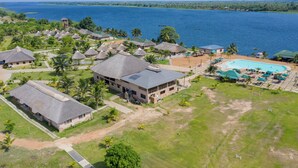 An aerial view of a resort with thatched-roof buildings, a swimming pool, and a large body of water in the background. - Sogakope Beach Resort & Spa (Sogakope)