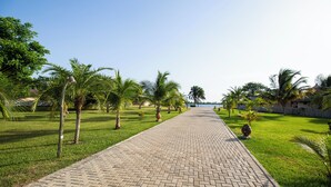 A paved pathway lined with palm trees and grass, leading towards a body of water. - Sogakope Beach Resort & Spa (Sogakope)