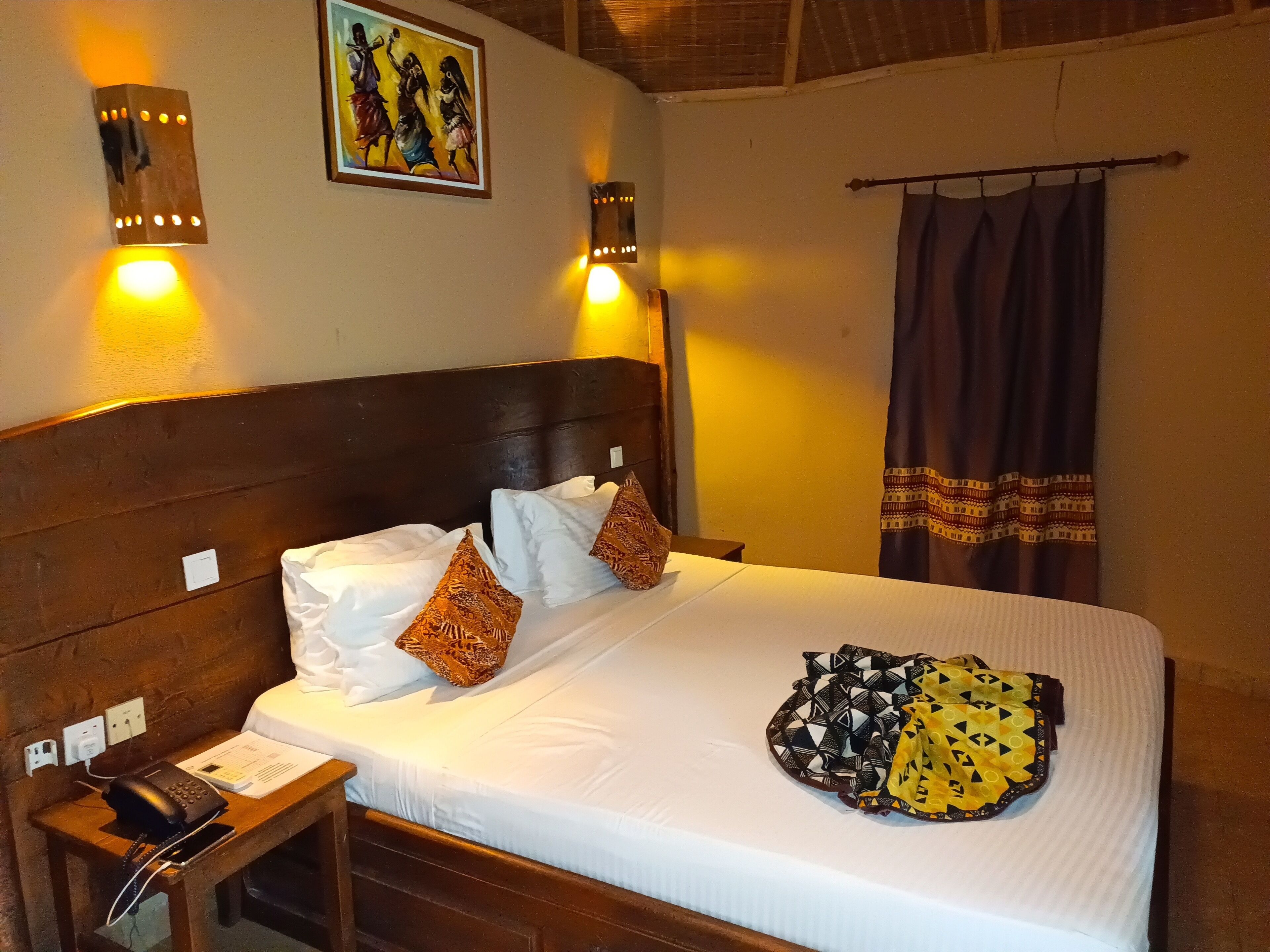 A neatly made bed with white and patterned pillows, a bedside telephone, and a wall-mounted light fixture.