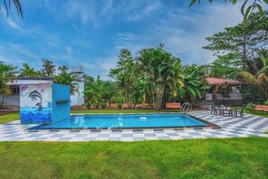 A swimming pool with a checkered pattern around it, surrounded by lush greenery and a mural of a dolphin. - Little Heaven Villa (Trimbak)