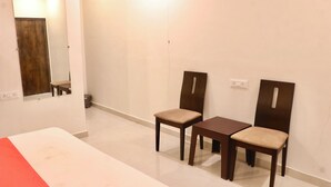 Una habitación con una cama, dos sillas de madera, una mesita, un espejo y una puerta.