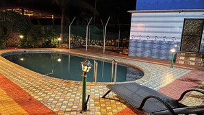 A swimming pool with a tiled deck, lounge chairs, and a mural of dolphins. - Lsq Sunita Farms (Karjat)