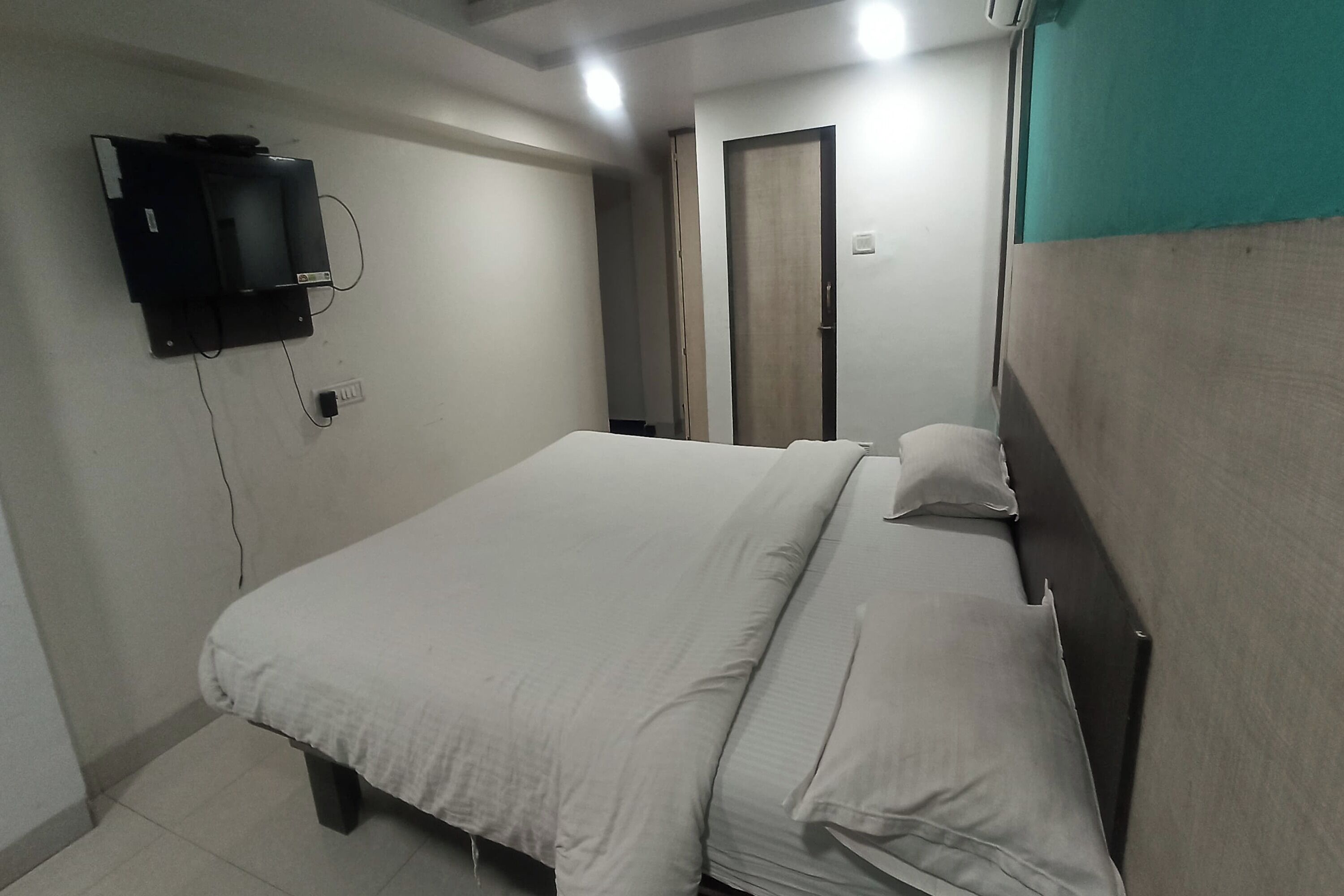 A bedroom with a bed, a television mounted on the wall, and a door in the background.