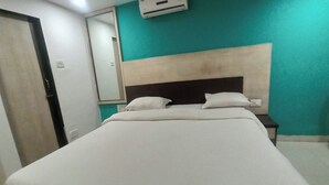 A neatly made bed with a headboard, a bedside table, and a wall-mounted air conditioner. - Hotel Blue Heaven (Mahabaleshwar)