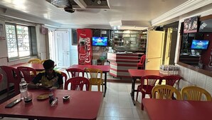 A restaurant with red tables and chairs, a Coca-Cola banner, and a television on the wall. - Hotel Blue Heaven (Mahabaleshwar)