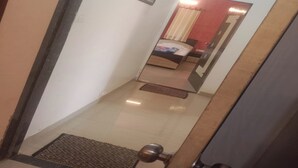 A narrow hallway leading to a bedroom with a bed, a mirror, and a door. - Devansh Villa (Mahabaleshwar)