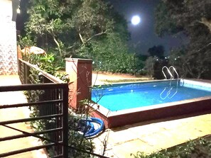 Une piscine éclairée la nuit, avec un escalier en métal et un tuyau d’arrosage enroulé à proximité.