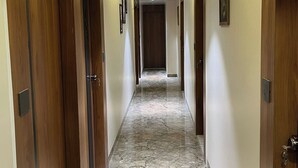 Un pasillo de hotel con puertas de madera, cuadros enmarcados en las paredes y suelo de mármol.