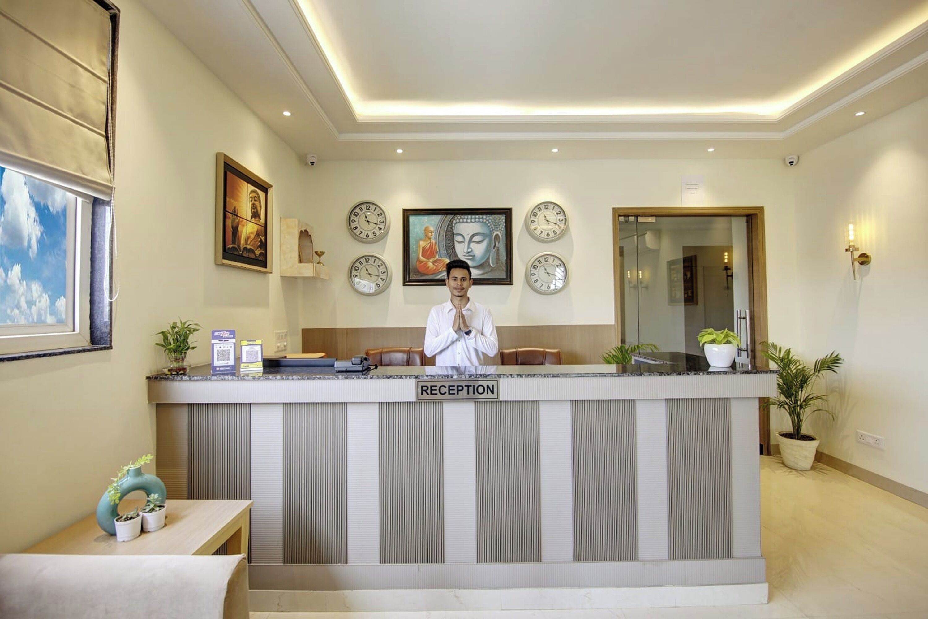 A reception desk with a sign, a receptionist, clocks, Buddha statues, and potted plants.