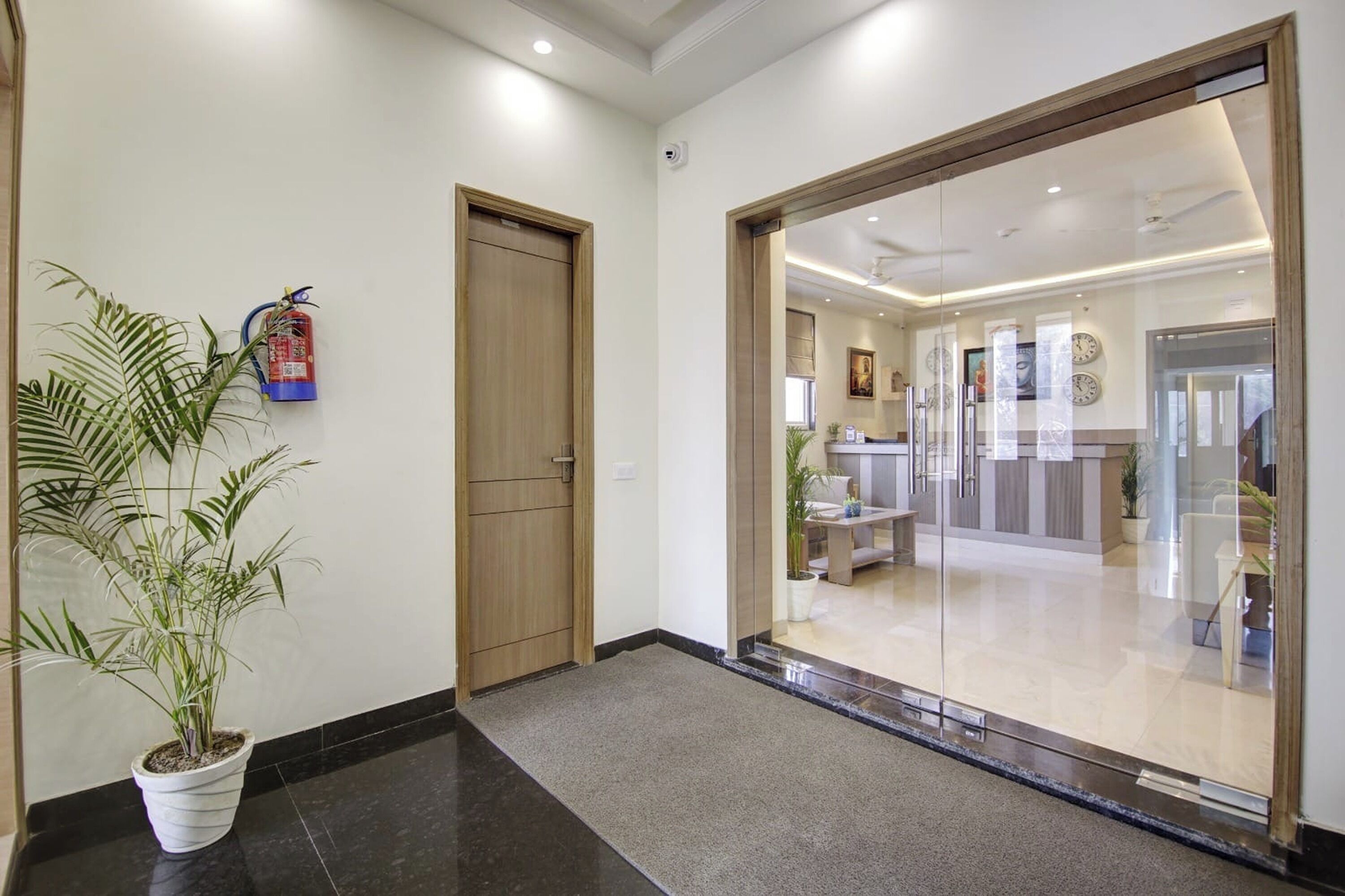 Un hall d’hôtel avec un comptoir d’accueil, un extincteur, une porte en bois et une plante en pot.