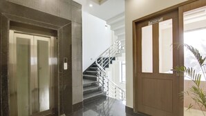 Un hall d’entrée moderne avec un ascenseur en marbre, un escalier doté de rampes en métal et une porte en bois portant l’inscription « Bureau du directeur ».