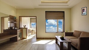 Un salon moderne comprenant un canapé, une table basse et un coin repas avec une table et des chaises. Une grande fenêtre offre une vue sur le ciel.