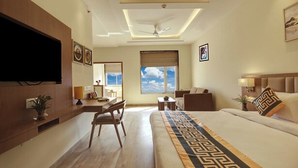 Une chambre d’hôtel avec un grand lit, un bureau, une chaise, une télévision et une fenêtre donnant sur le ciel.